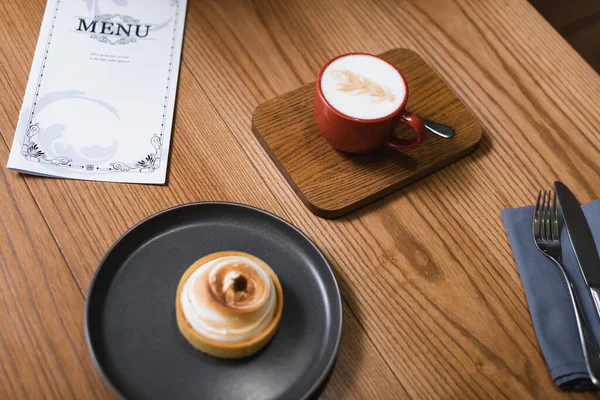 High angle view of lemon tart and cappuccino near menu on table — Stock Photo