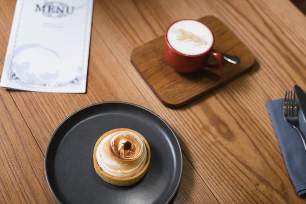 Vue grand angle de savoureuse tarte au citron et cappuccino près du menu sur table en bois — Photo de stock