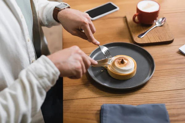 Vista recortada del hombre sosteniendo cubiertos cerca de tarta de limón en el plato - foto de stock