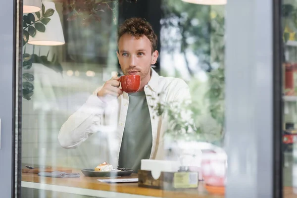 Curly man drinking coffee behind blurred window in cafe — Stock Photo