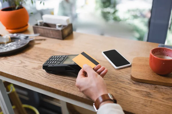 Ausgeschnittene Ansicht eines Mannes, der in der Nähe von Smartphone und Kaffeetasse im Café mit Kreditkarte bezahlt — Stockfoto