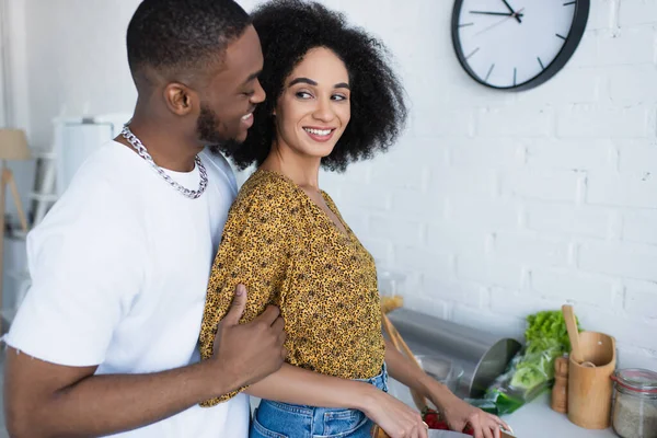 Jeune homme afro-américain étreignant sa petite amie avec un couteau dans la cuisine — Photo de stock