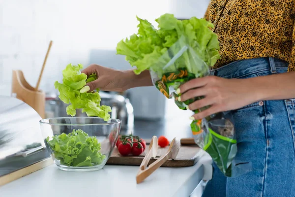 Vista recortada de una mujer afroamericana sosteniendo lechuga mientras cocina ensalada - foto de stock