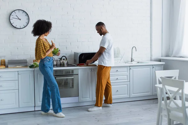 Vista lateral de la ensalada de cocina de pareja afroamericana en cocina - foto de stock