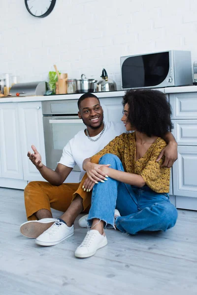 African american man talking to smiling girlfriend in kitchen — Stock Photo