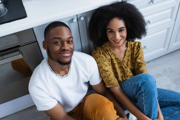 High angle view of young african american woman smiling at camera near boyfriend in kitchen — Stock Photo