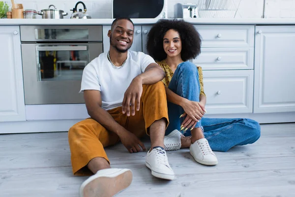 Sorrindo casal afro-americano sentado no chão na cozinha — Fotografia de Stock