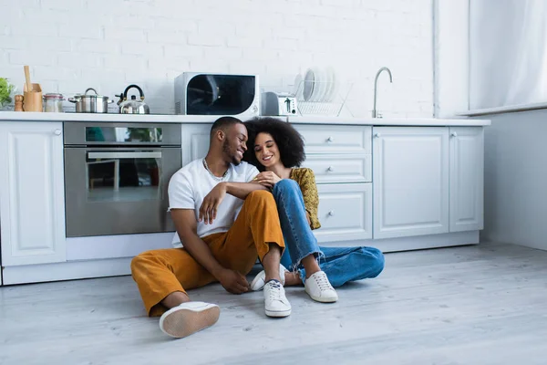 Uomo afroamericano seduto vicino sorridente ragazza sul pavimento in cucina — Foto stock