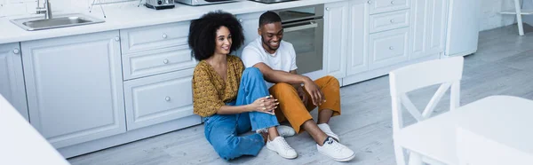 Jovem casal afro-americano sentado no chão na cozinha, banner — Fotografia de Stock