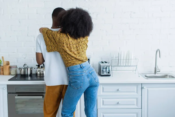 Vista posteriore della donna afro-americana che abbraccia il fidanzato in cucina — Foto stock