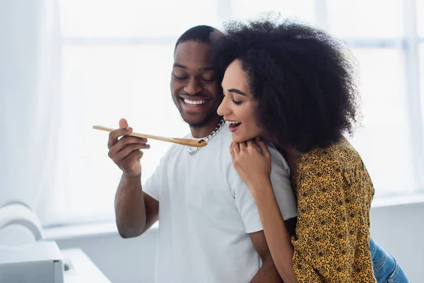 Smiling african american man holding spatula near girlfriend in kitchen — Stock Photo