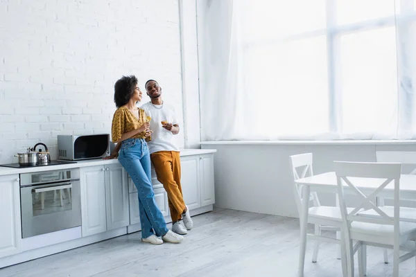 Souriant couple afro-américain tenant des verres avec du vin dans la cuisine — Photo de stock