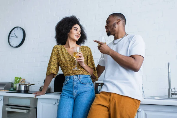 Couple afro-américain avec des verres de vin parlant près du plan de travail dans la cuisine — Photo de stock
