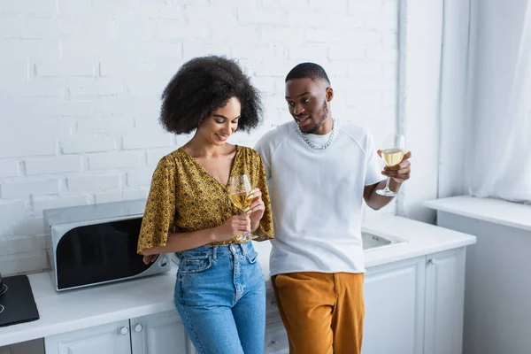 Young african american woman looking at glass of wine near boyfriend in kitchen — Stock Photo