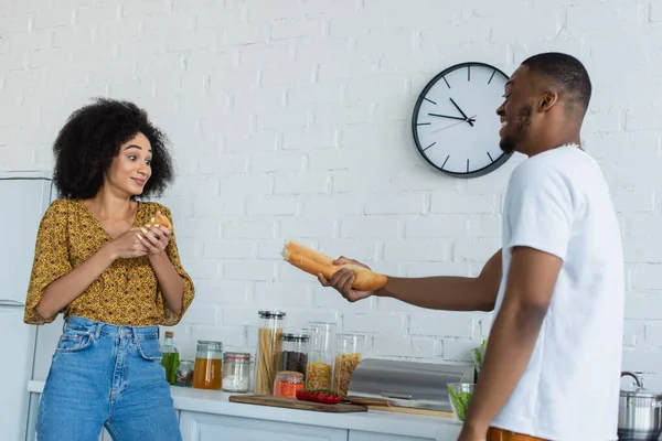 Africano americano uomo holding baguette vicino fidanzata in cucina — Foto stock