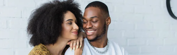 Sonriente mujer afroamericana abrazando novio en casa, pancarta - foto de stock