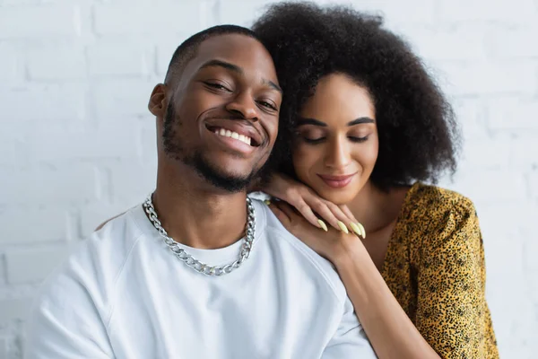 Sourire homme afro-américain regardant la caméra près de la petite amie à la maison — Photo de stock