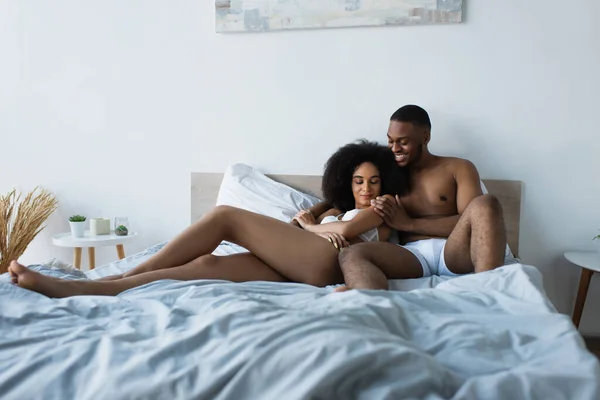 Joyeux homme afro-américain embrassant petite amie sexy sur le lit — Photo de stock
