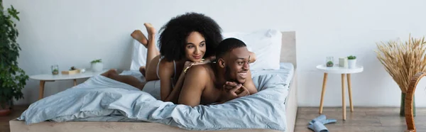 Mujer en ropa interior acostada en la sonrisa afroamericana novio en la cama, pancarta - foto de stock