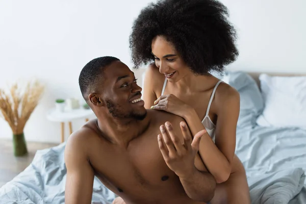 Sorridente donna africana americana in reggiseno abbracciare fidanzato sul letto — Foto stock