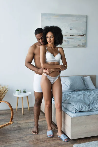 African american man hugging girlfriend in lingerie in bedroom — Stock Photo