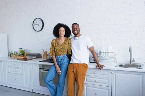 Alegre casal afro-americano olhando para a câmera na cozinha — Fotografia de Stock