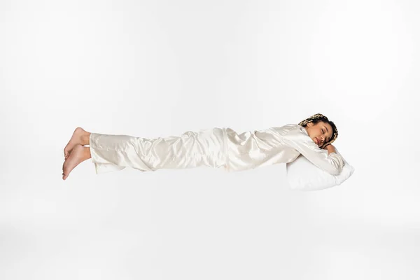 Visão de comprimento total da mulher americana africana descalça em pijama de seda dormindo enquanto levita isolado no branco — Fotografia de Stock