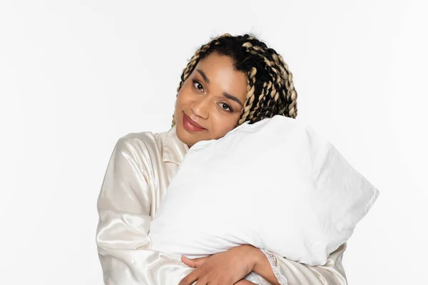 Femme afro-américaine positive souriant à la caméra tout en embrassant oreiller isolé sur blanc — Photo de stock