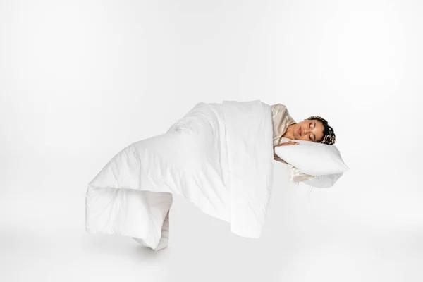 Afrikanische Amerikanerin schläft auf Kissen unter Decke, während sie auf weißer Erde schwebt — Stockfoto