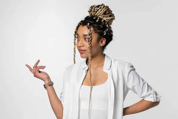Giovane donna d'affari afroamericana con dreadlocks distogliendo lo sguardo e indicando con dito isolato su bianco — Foto stock