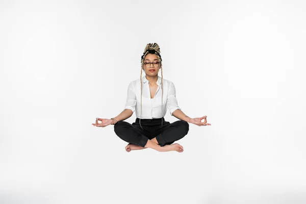 Mulher de negócios afro-americana com olhos fechados levitando durante a meditação em pose de lótus isolada em branco — Fotografia de Stock