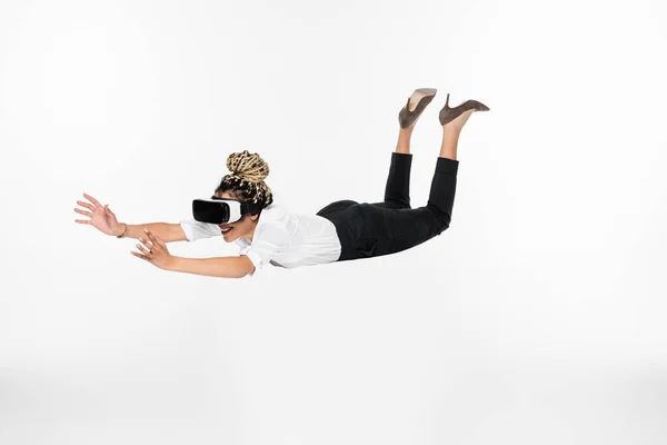 Счастливая африканская американская деловая женщина, играющая в виртуальные наушники, в то время как левитация изолированы на белом — стоковое фото