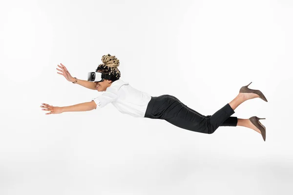 Vista lateral de la alegre mujer de negocios afroamericana volando en auriculares vr aislados en blanco - foto de stock