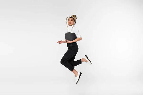 Cheerful african american businesswoman looking at camera while levitating with paper folder isolated on white — Stock Photo