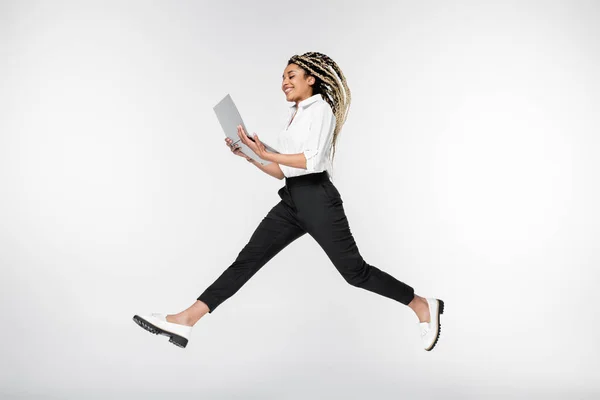Счастливая африканская американская бизнесвумен левитации с ноутбуком изолированы на белом — стоковое фото