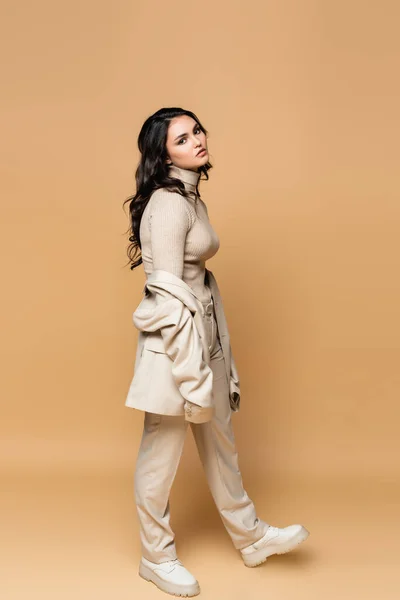 Full length of brunette model in turtleneck and suit posing on beige — Stock Photo