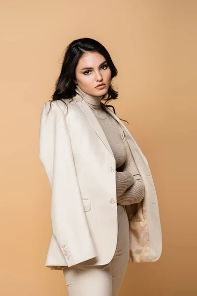 Pretty model in turtleneck and blazer posing with crossed arms isolated on beige — Stock Photo