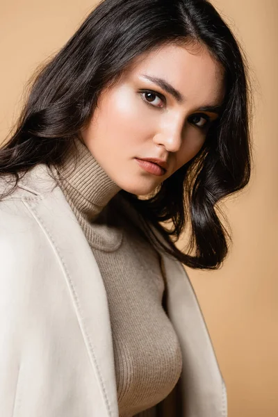 Brunette and pretty model in turtleneck looking at camera isolated on beige — Stock Photo