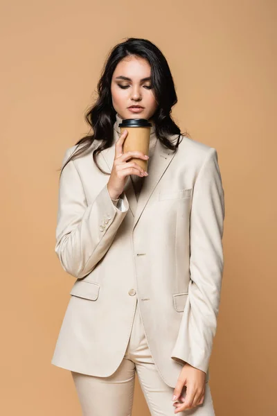 Young pretty woman in turtleneck and suit holding paper cup isolated on beige — Stock Photo