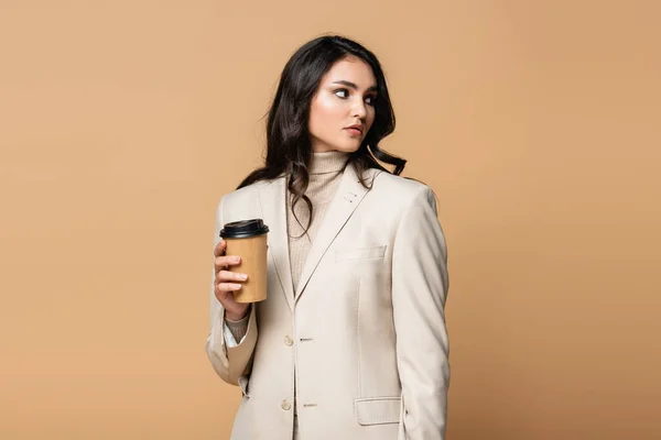 Young woman in turtleneck and blazer holding paper cup isolated on beige — Stock Photo
