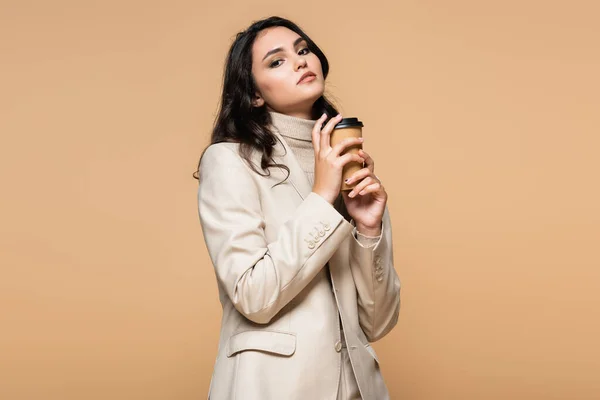 Jeune joli modèle à col roulé et blazer tenant tasse en papier isolé sur beige — Photo de stock