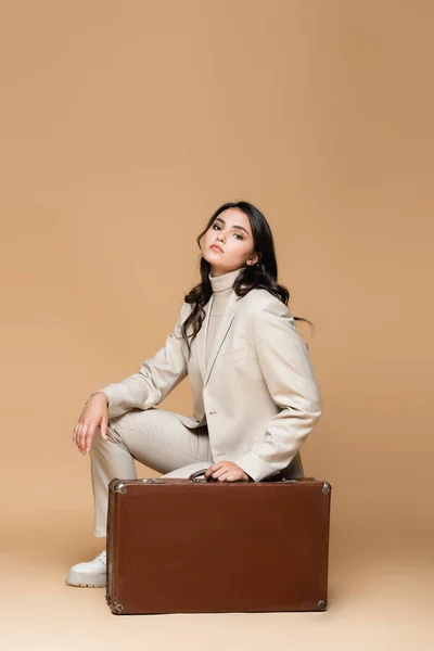 Young traveler in suit posing near vintage suitcase on beige — Stock Photo