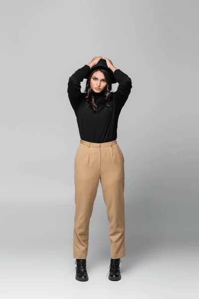 Pleine longueur de jeune femme élégante en chapeau fedora posant sur gris — Photo de stock