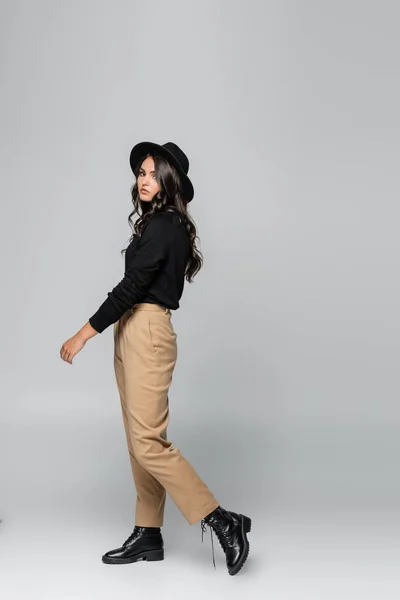 Longitud completa de la mujer joven de moda en sombrero fedora posando en gris - foto de stock