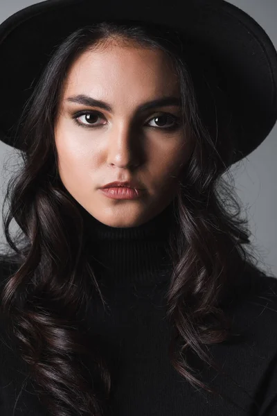Brunette model in black fedora hat and turtleneck looking at camera isolated on grey — Stock Photo