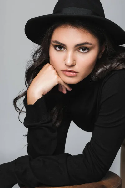 Young brunette woman in fedora hat looking at camera isolated on grey — Stock Photo