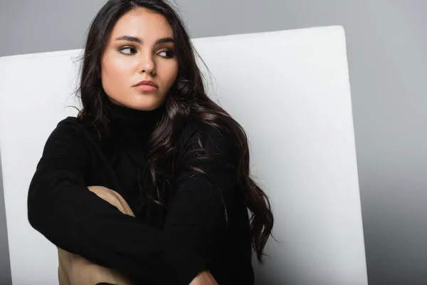 Stylish model in black turtleneck looking away near white cube isolated on grey — Stock Photo