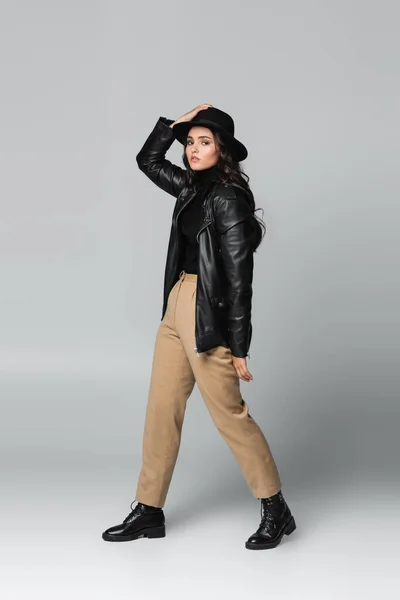 Trendmodel in voller Länge mit Fedora-Hut und schwarzer Lederjacke posiert auf grau — Stockfoto