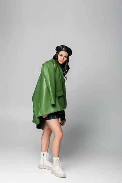 Повна довжина молодої жінки в береті, плетеній спідниці і зеленій куртці позує на сірому — Stock Photo