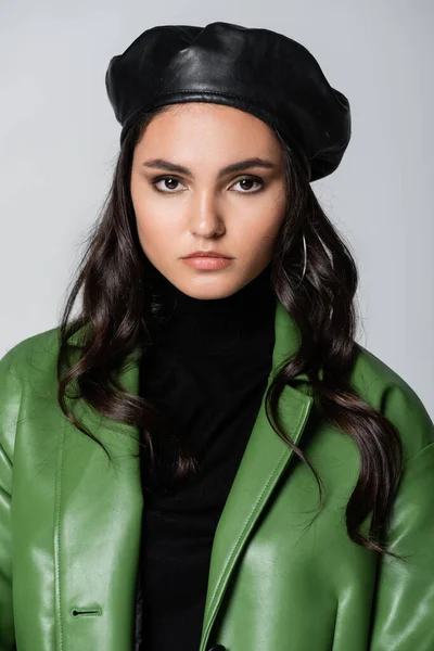 Modelo joven en cuello alto negro, chaqueta verde y boina mirando a la cámara aislada en gris - foto de stock